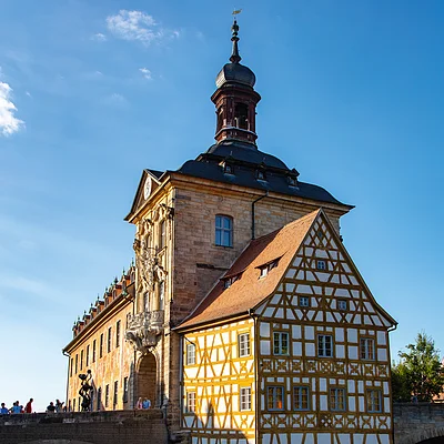 Historisches Fachwerkhaus mit Turm auf einer Steinbrücke über einen Fluss bei blauem Himmel.