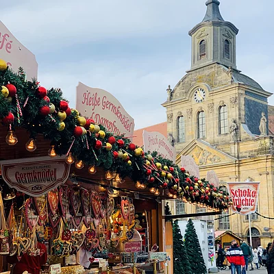 Weihnachtsmarktstand mit Lebkuchenherzen und Dekoration vor historischer Kirche und Passanten auf Pflasterstraße