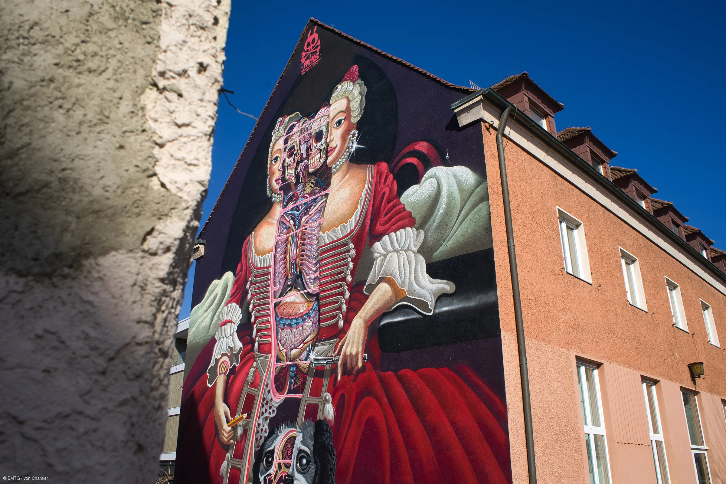 Wandgemälde einer historischen Frau mit teilweise sichtbaren inneren Organen an der Fassade eines Gebäudes.