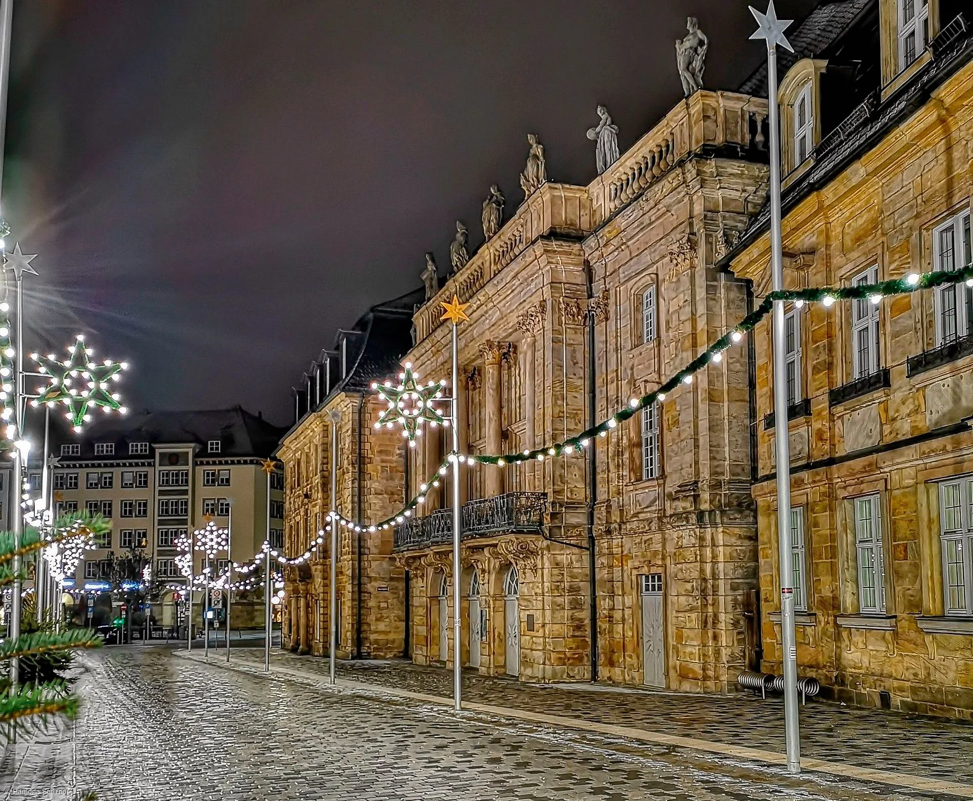 Beleuchtete Straße mit historischen Gebäuden und Weihnachtsstern-Dekoration bei Nacht.