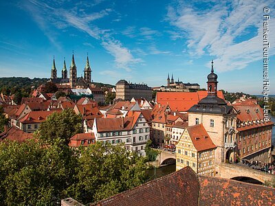 Eine Stadtansicht mit historischen Gebäuden, Kirchtürmen und Brücken bei blauem Himmel
