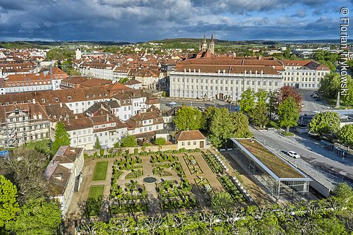Stadtbild von oben (Ansbach, Romantisches Franken) Luftaufnahme eines barocken Gartens mit angrenzenden historischen Gebäuden und Stadt im Hintergrund bei bewölktem Himmel.