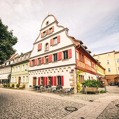 Historische Fachwerkhäuser mit roten Fensterläden an gepflasterter Straße unter bewölktem Himmel.