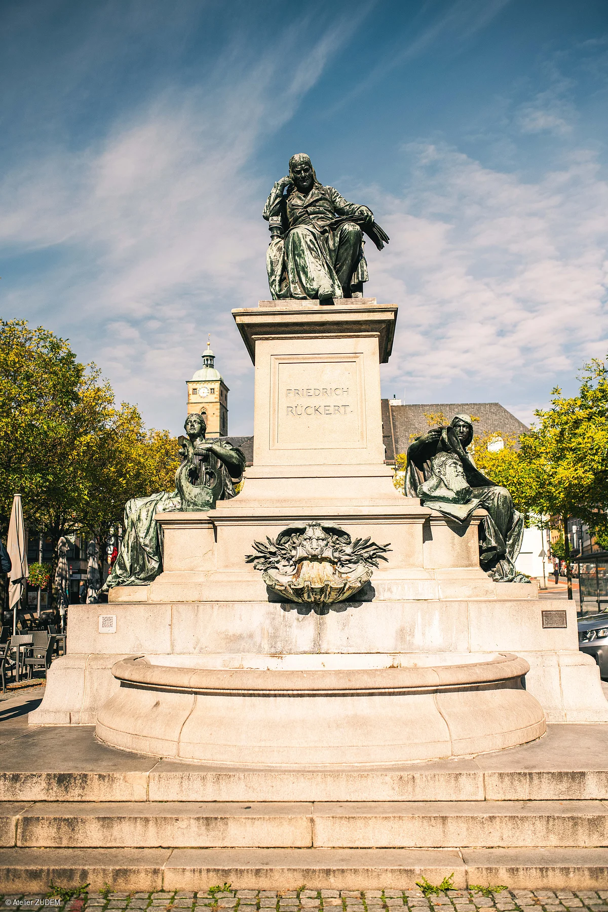 Denkmal von Friedrich Rückert mit drei Figuren auf einem steinernen Sockel im Freien bei Tageslicht