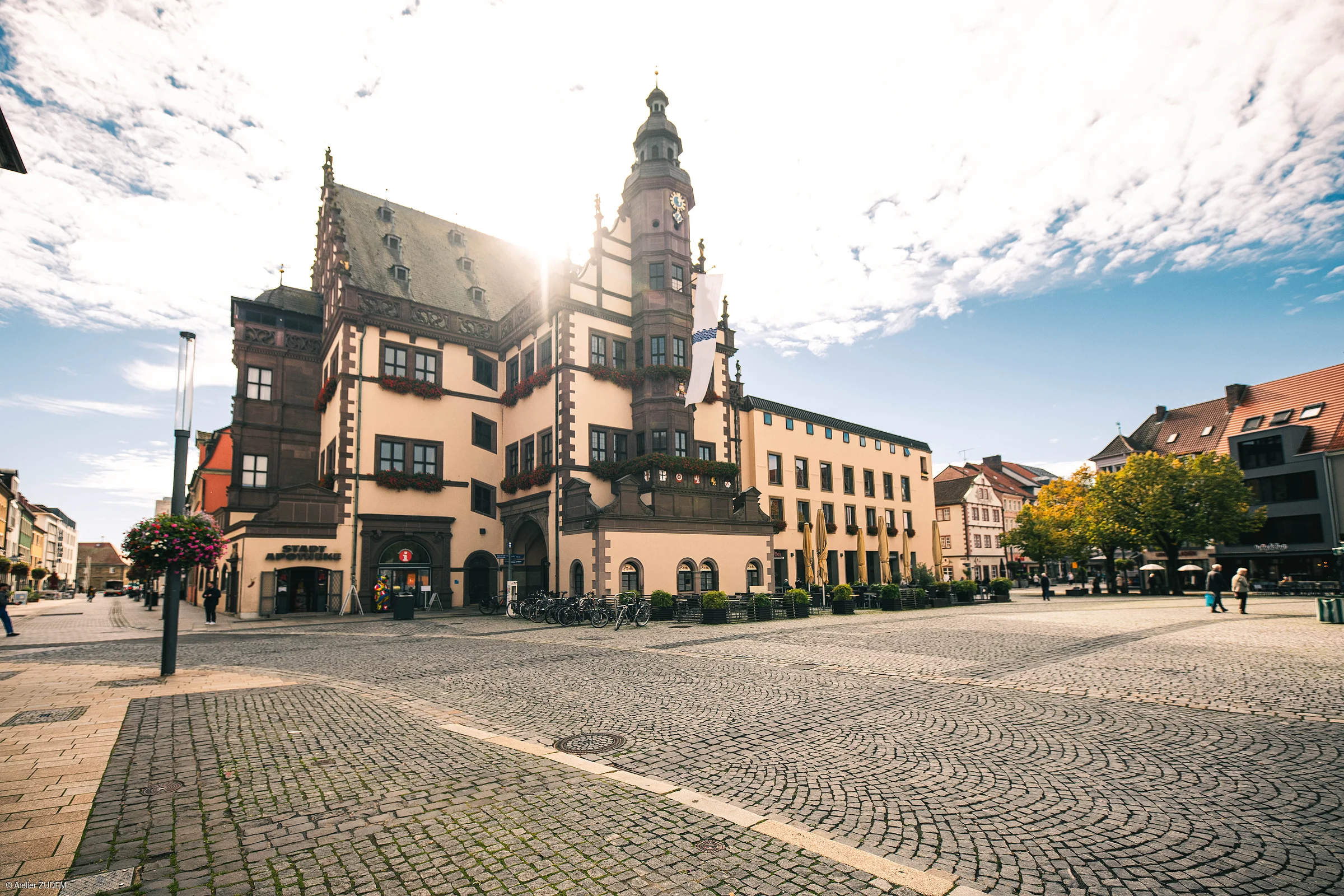 Historisches Rathaus mit Turm an einem großen gepflasterten Marktplatz bei Sonnenschein und blauem Himmel.