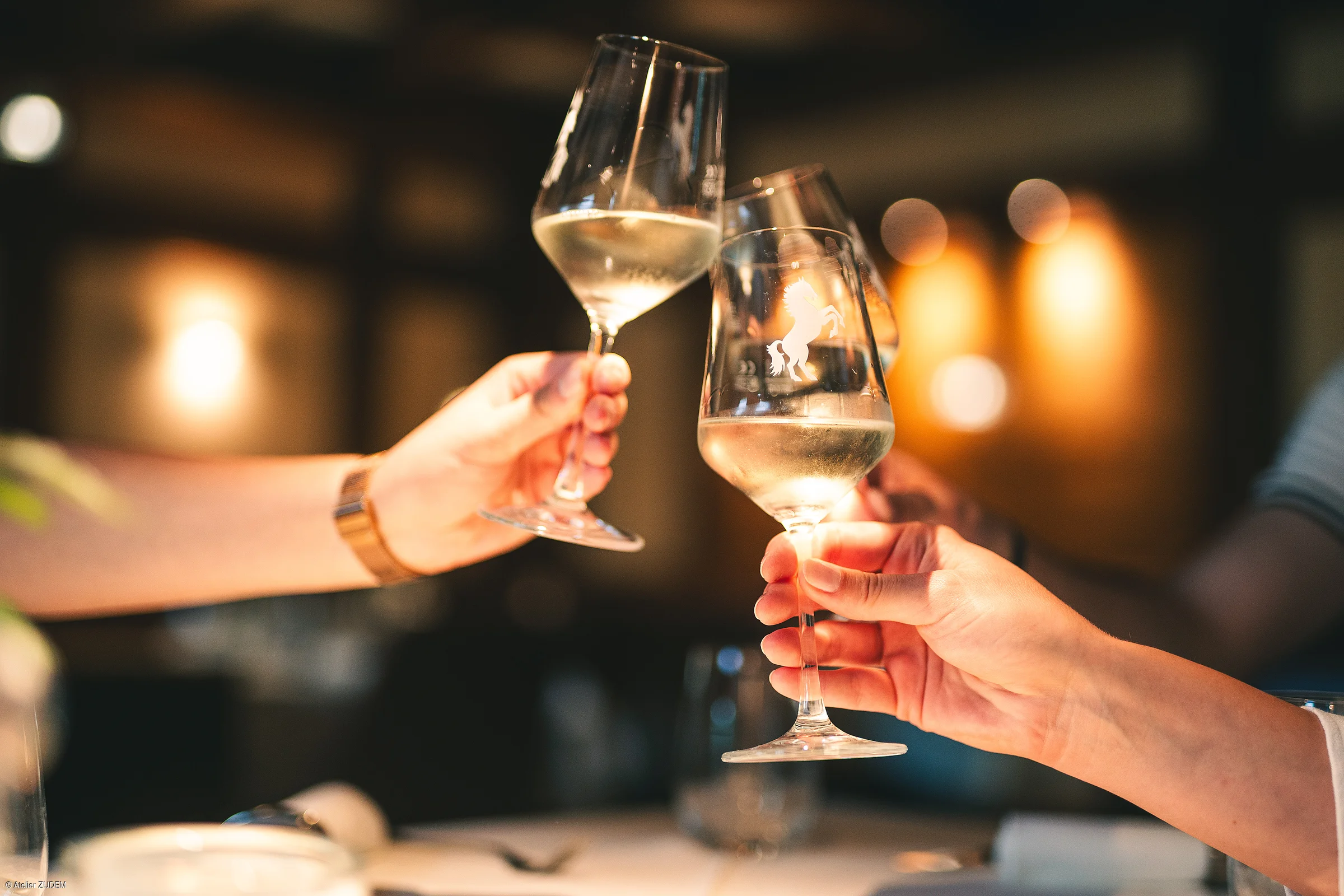 Drei Hände stoßen mit gefüllten Weingläsern in einem Restaurant an, unscharfer Hintergrund.