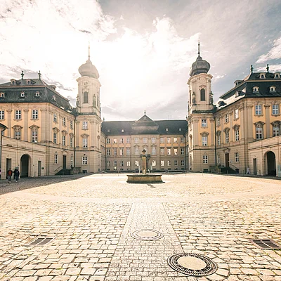 Innenhof eines historischen Gebäudes mit Kopfsteinpflaster und Brunnen in der Mitte bei Sonnenschein