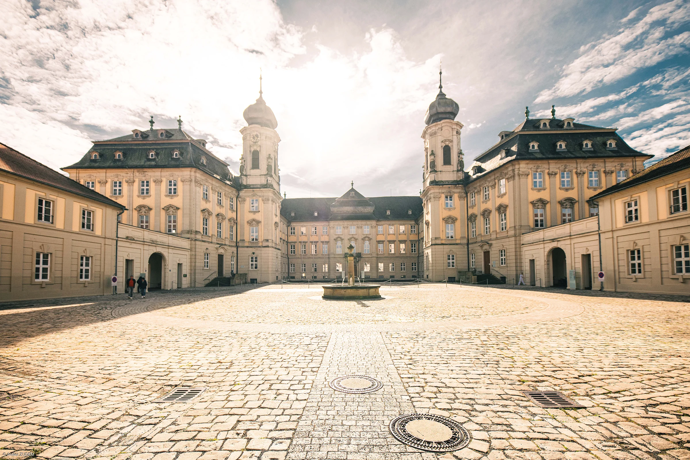 Innenhof eines historischen Gebäudes mit Kopfsteinpflaster und Brunnen in der Mitte bei Sonnenschein